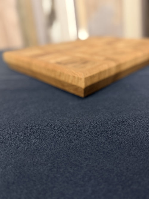 A close-up shot of a dark navy blue textured fabric surface with a wooden board placed diagonally on top, photographed in soft focus with the front edge in sharp detail.